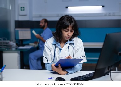 Professional medic looking at computer screen and medical files for healthcare. Doctor analyzing information on monitor and taking notes on papers for assistance, doing overtime work.