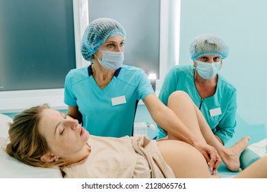 Professional Medical Staff And Doctor Help A Pregnant Woman In Childbirth In Hospital. Female Doctor Listening To Fetal Heartbeat, Using A Doppler Sonogram, Connection, Wearing A Mask.