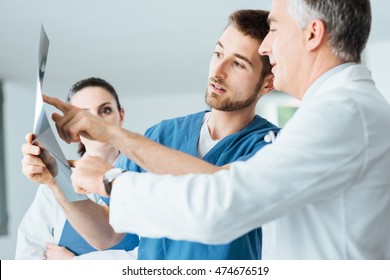 Professional medical team with doctors and surgeon examining patient's x-ray image, discussing and pointing - Powered by Shutterstock