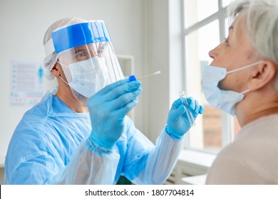 Professional medical worker wearing personal protective equipment testing senior woman for dangerous disease using test stick