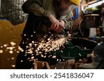 Professional metalworker in protective workwear bending over workbench with metal detail while grinding it in workshop