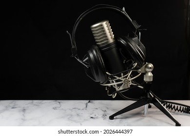 Professional microphone with black headphones over black background on white marble table