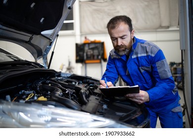 Professional middle aged caucasian car mechanic with checklist standing by vehicle engine area with hood open detecting malfunction. - Powered by Shutterstock