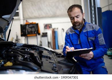 Professional middle aged caucasian car mechanic with checklist standing by vehicle engine area with hood open detecting malfunction. - Powered by Shutterstock