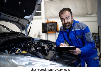 Professional middle aged caucasian car mechanic with checklist standing by vehicle engine area with hood open detecting malfunction. - Powered by Shutterstock