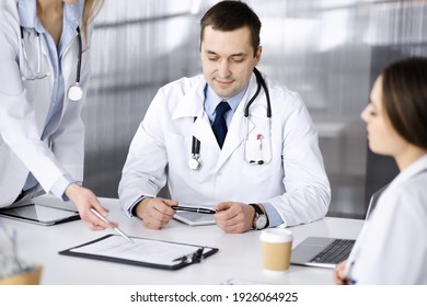 Der professionelle Arzt mittleren Alters spricht mit seinen Kollegen, während er im Krankenhaus am Schreibtisch sitzt. Ärzteteam, das die Ergebnisse der Blutprobe in einer Klinik diskutiert. Medizin und Gesundheitswesen