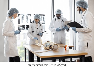 Professional middle aged Indian female doctor, anatomy teacher, explaining bones anatomy using skeleton model for diverse students in white coats. Medicine, education, anatomy concept. - Powered by Shutterstock