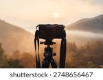 Professional mirrorless camera setup on tripod capturing golden sunrise over foggy valley in tropical rainforest at countryside