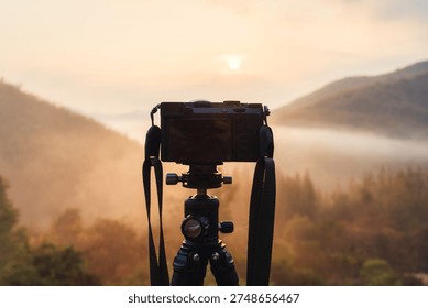 Professional mirrorless camera setup on tripod capturing golden sunrise over foggy valley in tropical rainforest at countryside