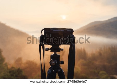 Professional mirrorless camera setup on tripod capturing golden sunrise over foggy valley in tropical rainforest at countryside