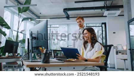 Professional mixed-raced managers analyzing or comparing important information on computer. Handsome man standing besides woman and helping her completing working task. Cooperation concept.