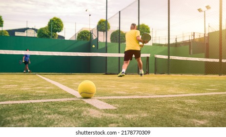 Professional Monitor Of Padel Jump To The Ball With A Black Racket. Class To Student On Outdoor Tennis Court. Man Paddel Player Playing A Match In The Open. Racquet Sport Game Concept.