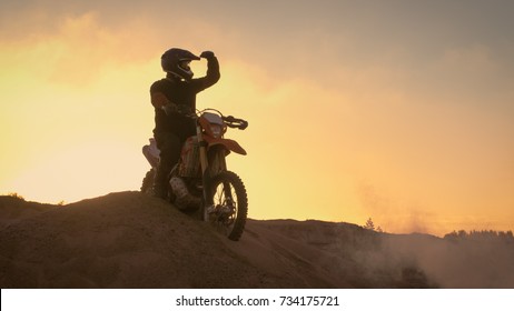 Professional Motocross Biker Spectacularly Stands on the Off-Road Dune on his Enduro Motorcycle. Looks Afar on the Whole Track.