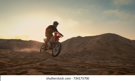 Professional Motocross Motorcycle Rider Driving Over the Dune and Further Down the Off-Road Track. It's Sunset and Track is Covered with Smoke/ Mist. - Powered by Shutterstock