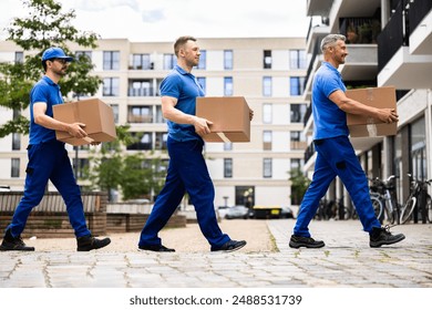 Professional movers are loading a van with boxes to deliver to a new house. The certified driver is carrying furniture.