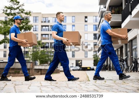 Professional movers are loading a van with boxes to deliver to a new house. The certified driver is carrying furniture.
