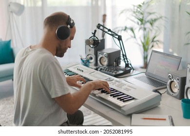 Professional musician composing music at home, he is wearing headphones and playing a digital piano - Powered by Shutterstock