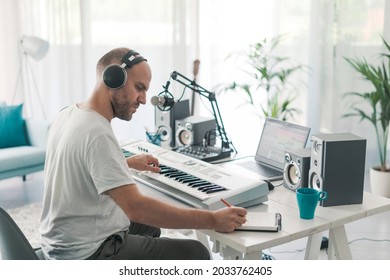 Professional Musician Sitting At Desk And Composing A New Song, He Is Writing Notes On A Music Sheet