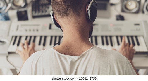 Professional musician wearing headphones and playing the keyboard, he is composing a new song