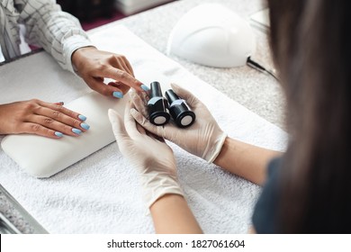 Professional Nail Care And Reopening Of Beauty Studio During Epidemic. African American Woman Client Chooses Gel Polish In Hands Of Master In Rubber Gloves In Modern Salon With Equipment, Above View