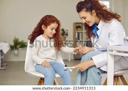 Professional neurologist examining happy child. Friendly female doctor holding cute little girl by hand and using hammer to test knee jerk patellar reflex. Health, neurology, medical checkup concept