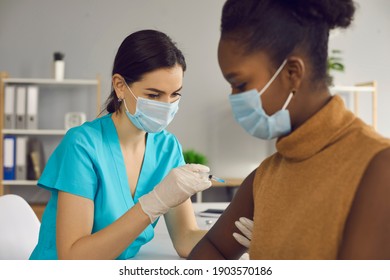 Professional nurse or doctor in medical face mask and gloves giving flu vaccine injection to female patient. Young woman getting COVID-19 shot during vaccination campaign in modern clinic or hospital