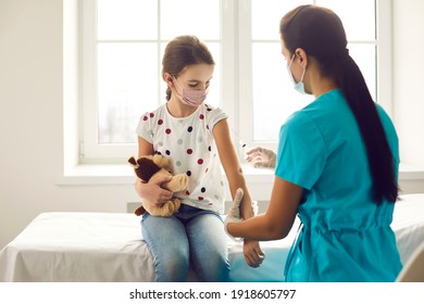 Professional Nurse Giving Shot To Little Kid. Doctor Injecting Child With Flu Or Covid 19 Vaccine. Girl In Medical Face Mask Holding Favorite Toy And Getting Injection At Clinic. Immunization Concept