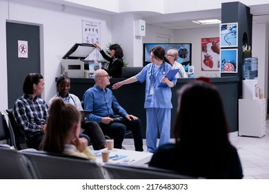 Professional Nurse Taking Older Patient To See Doctor For Clinic Appointment While African American Medic Is Completing Form For Asian Young Man. Diverse People Waiting In Private Practice Hospital.