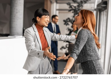 A professional office environment featuring two cheerful colleagues sharing a happy embrace, expressing positivity. Other workers visible in the background enhance the warm and collaborative atmosphere.