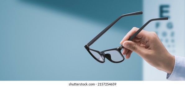 Professional optometrist holding glasses and eye chart in the background, eyesight and vision problems concept, copy space - Powered by Shutterstock