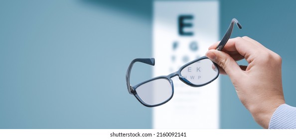 Professional optometrist holding glasses and eye chart in the background, eyesight and vision problems concept, copy space