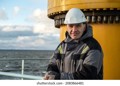 A Professional In Overalls. Shift Worker Of The Arctic Oil Platform. On His Head Is The White Helmet Of The Master.