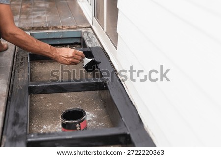 A professional painter is applying anti rust paint to a steel balcony outside a house.