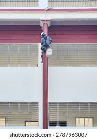 Professional painter using a safety harness and rope access to paint a tall exterior pillar on a residential building facade.