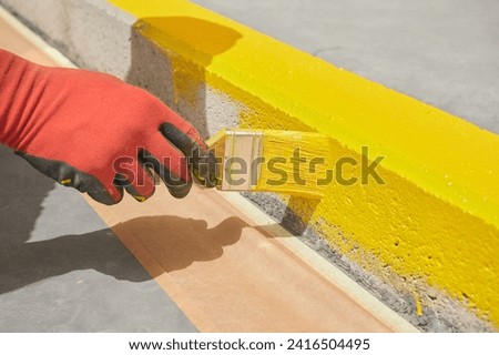 Professional painter at work. Unrecognizable young man uses a paint brush to apply special acrylic paint for road marking on kerbstone.