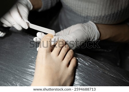 Professional pedicure in progress, the master cleans and files nails with a nail file, dry pedicure