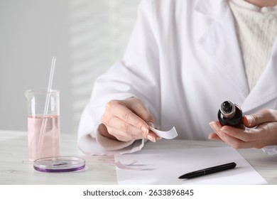 Professional perfumer developing luxury perfume at white wooden table in laboratory, closeup