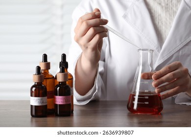 Professional perfumer developing luxury perfume at wooden table in laboratory, closeup