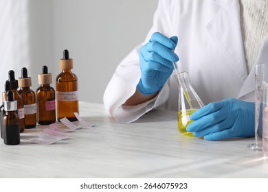 Professional perfumer developing luxury perfume at white wooden table in laboratory, closeup