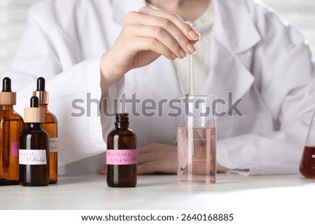 Professional perfumer developing luxury perfume at white wooden table in laboratory, closeup