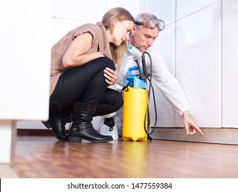 A Professional Pest Control Contractor Or Exterminator Squads With The Young Female Customer In The Kitchen On The Ground And Show Her Problems With Mold Pests Bugs And Have A Chemical Container