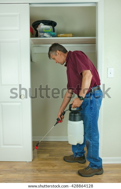A professional pest control service man or\
do-it-yourself home owner spraying pesticide on the inside of a\
house to keep bugs out.