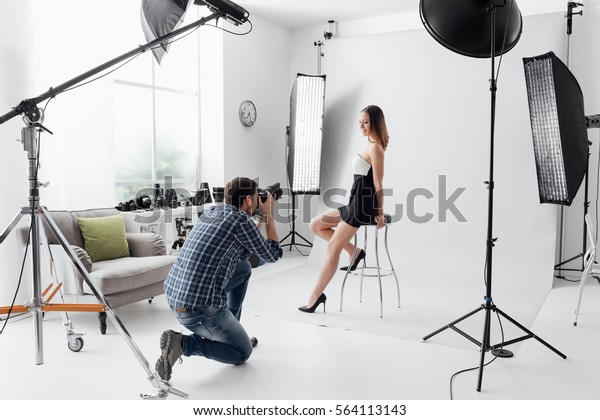 Professional photo shooting at the studio: a\
beautiful young model is smiling and posing; the photographer is\
taking pictures with a digital\
camera
