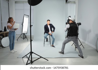 Professional photographer with assistant taking picture of young man in modern studio - Powered by Shutterstock