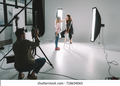 professional photographer, makeup artist and beautiful model on fashion shoot in photo studio with lighting equipment  