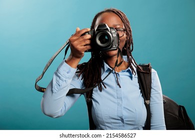 Professional photographer with photographing modern device taking pictures while looking at camera on blue background. Creative photograpy entusiast enjoying leisure time while shooting photos.