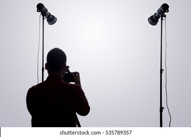 Professional photographer. Portrait of confident young man in shirt holding hand on camera while standing against grey background