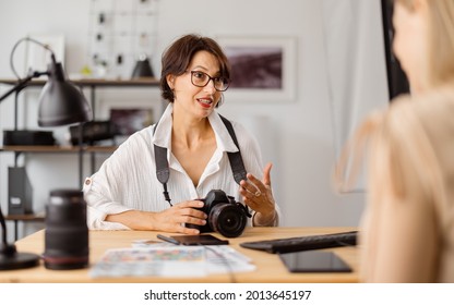 Professional photographer sitting at bright office and talking with client about photo session.Two women discussing working details indoors.