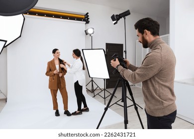 Professional photographer and stylist working with beautiful model in modern photo studio
