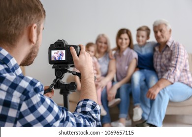 Professional Photographer Taking Photo Of Family On Sofa In Studio